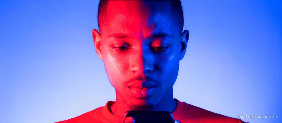 A young South African man staring at his phone with a slightly puzzled look, as if trying to remember something