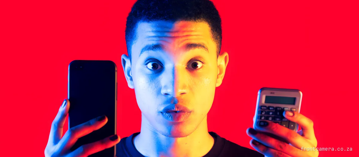 A young South African creator holding a phone in one hand and a pocket calculator in the other, eyebrows raised