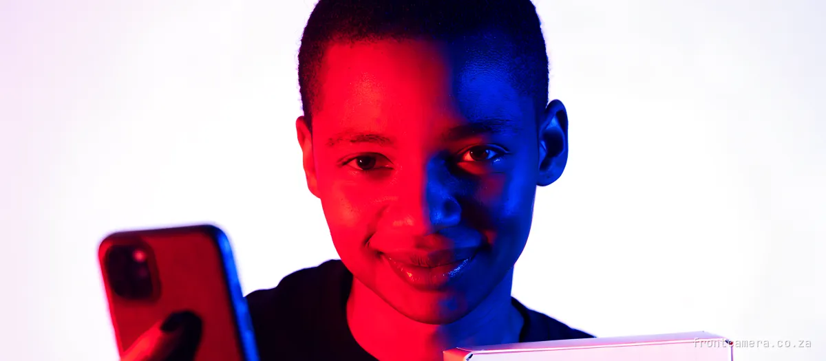 A South African creator holding a gifted product box under one arm and a phone in the other hand, wry half-smile