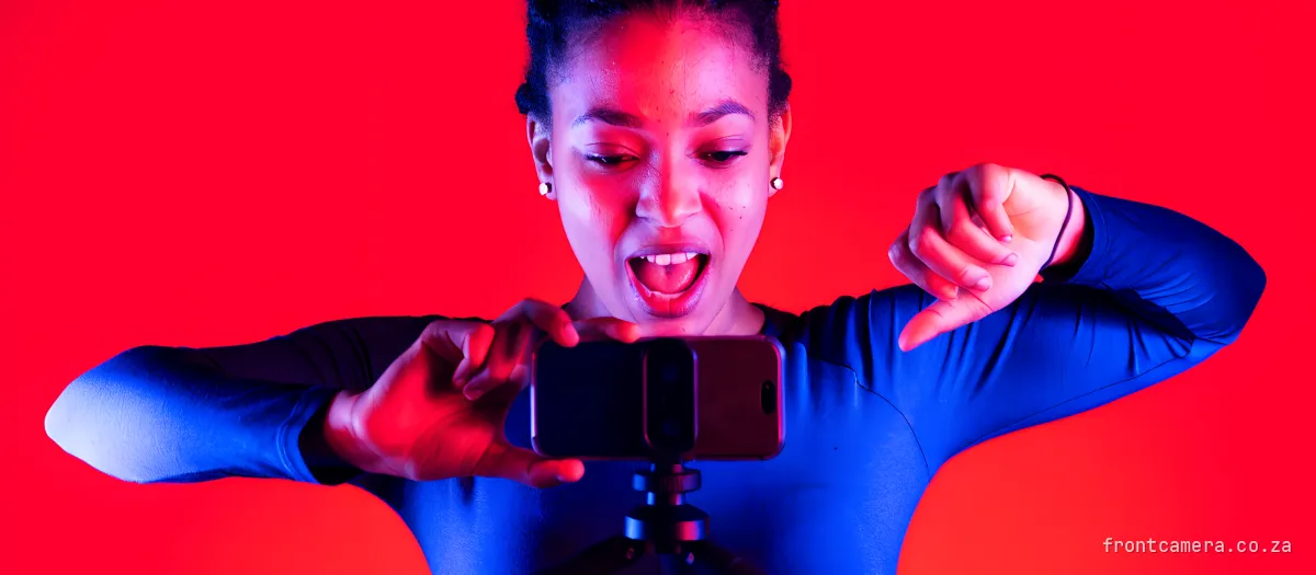 A young South African woman filming herself on a phone mounted on a small tripod, mid dance move, energetic
