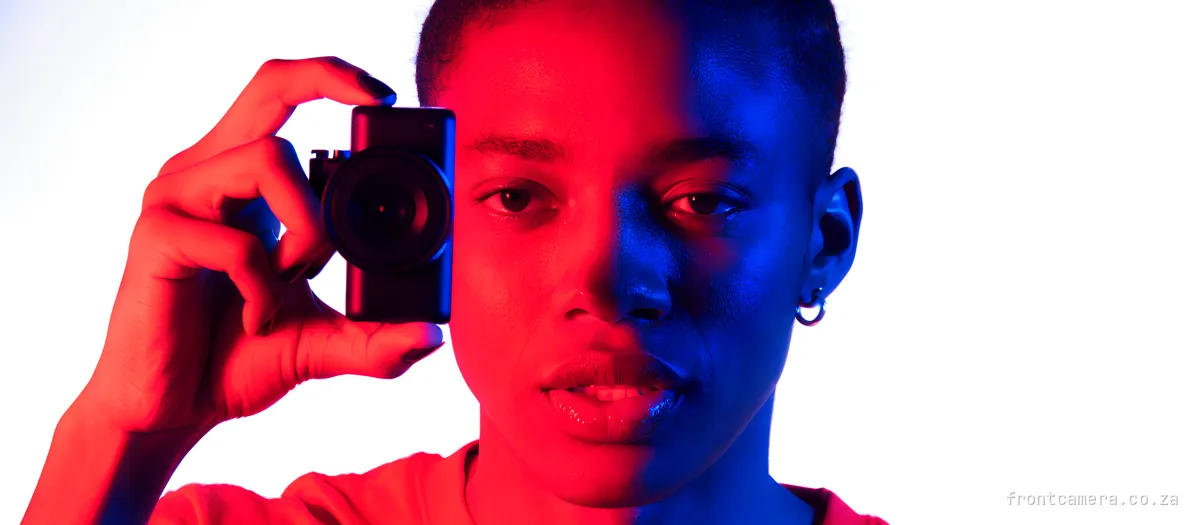 A South African video creator holding a compact camera up beside their face, looking into the lens